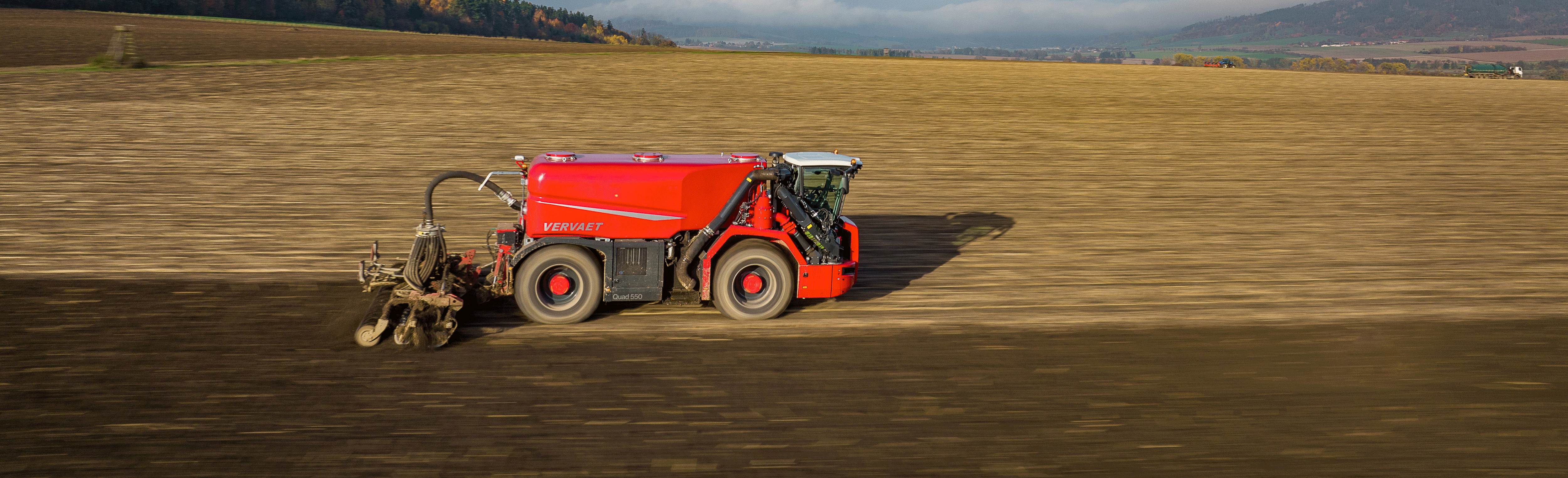 Červený traktor s jednoosou cisternou na poli